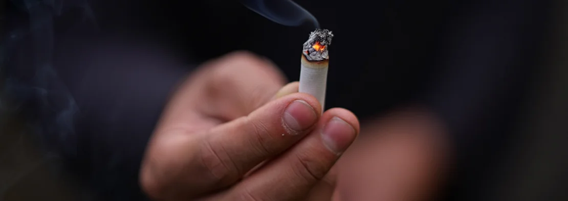 Рука держит тлеющую сигарету